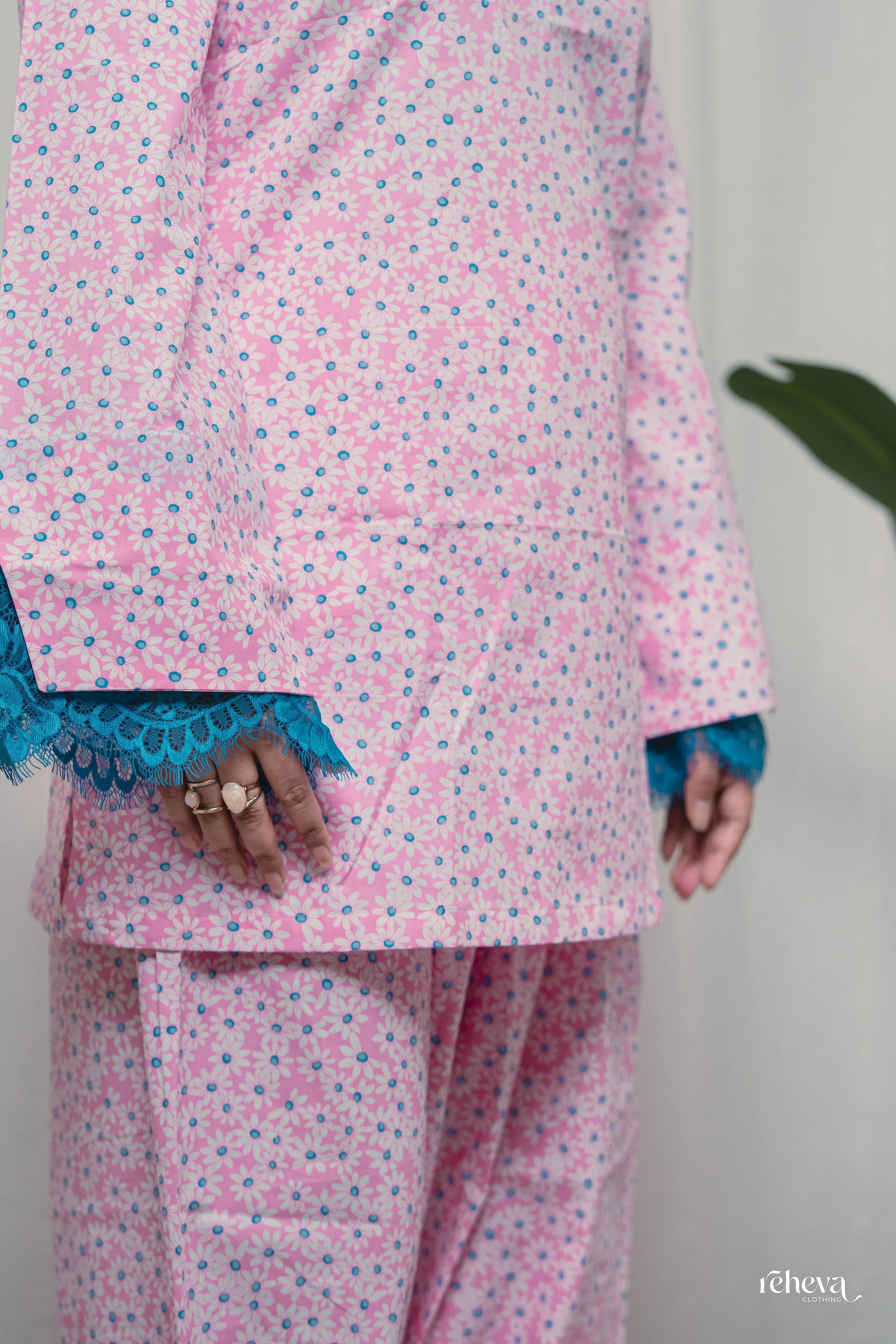 A person wearing a pink and blue floral print pajama set with blue lace trim on the cuffs, shown from the chest down against a light background.